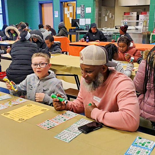 Family Bingo Night Families seated at tables playing bingo together during a community event at Penrose Elementary.
